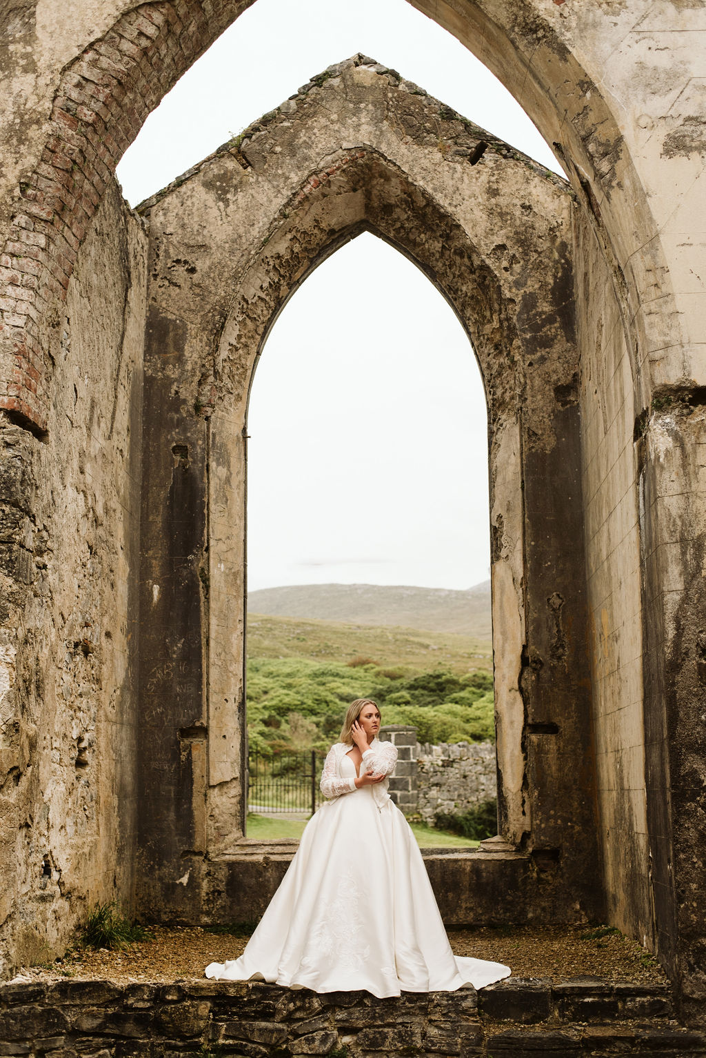 Bride standing in the abandoned altar area of Dunlewey Church wearing a mikado ballgown wedding dress and lace bomber jacket in Ireland