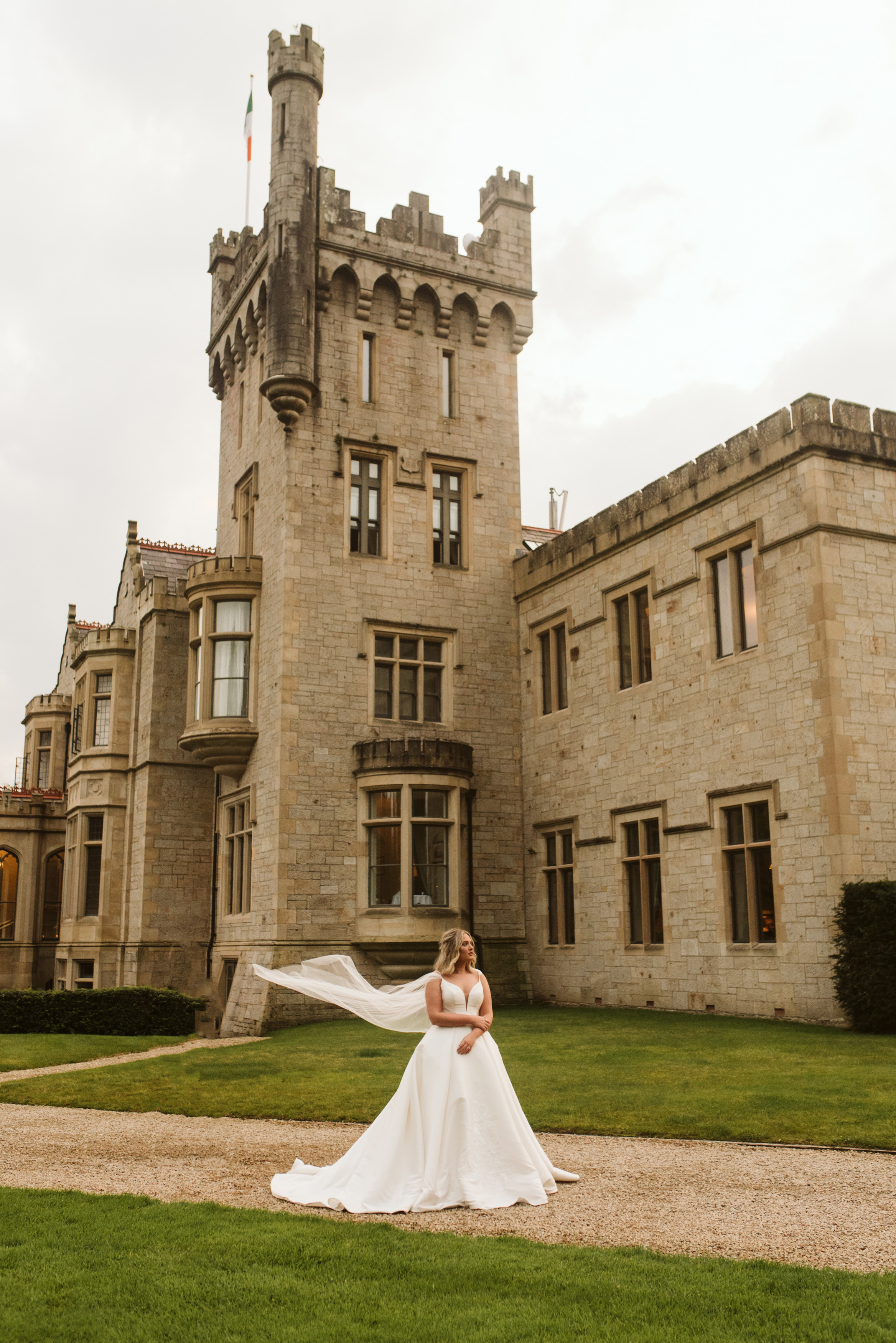 Bride in a mikado ballgown wedding dress with a tulle cape blowing in the wind at Lough Eske Castle in Ireland