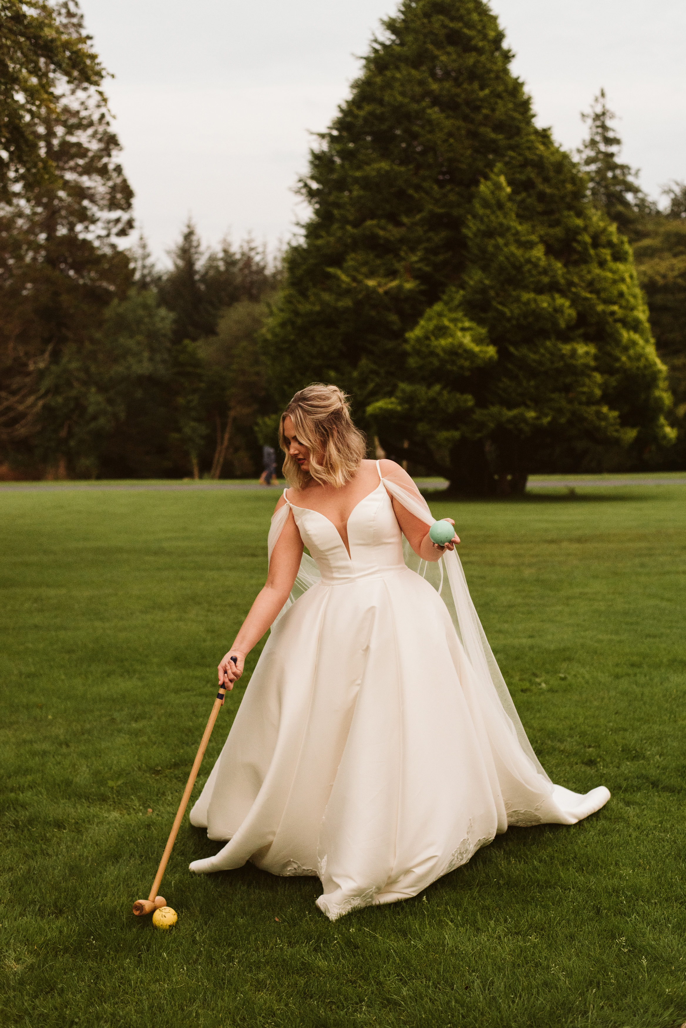Bride playing croquet in a mikado ballgown wedding dress with straps and a tulle cape on the grounds of Lough Eske Castle in Ireland