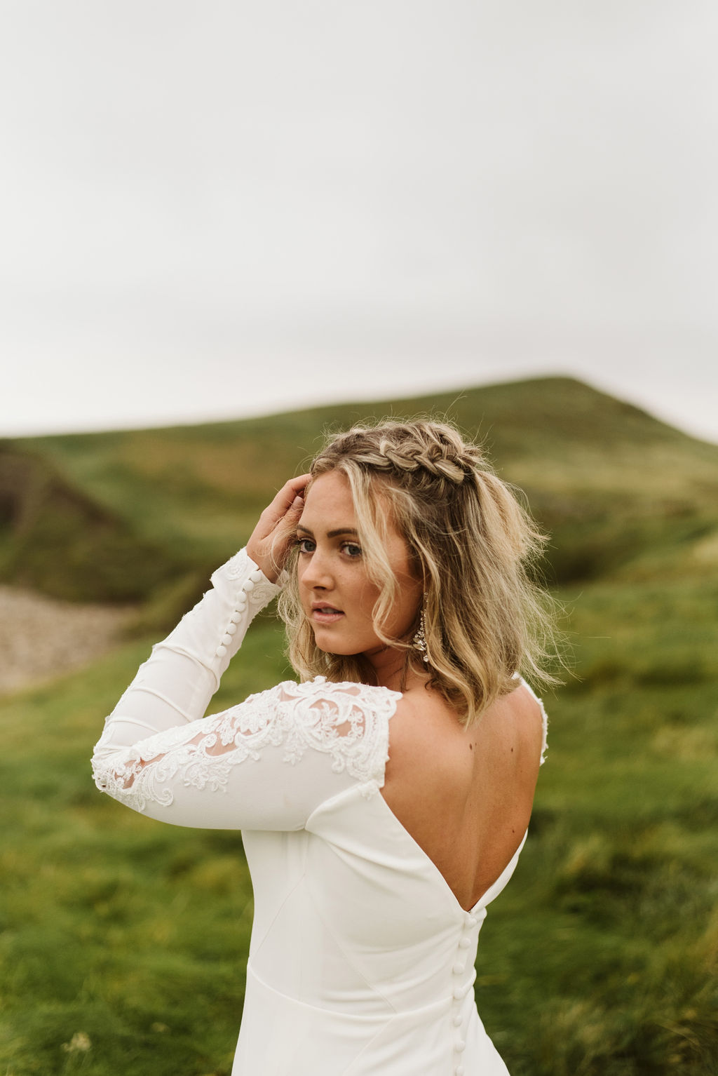 Close up view of bride wearing a fitted crepe wedding dress with long sleeves, sparkly earrings and braids in her hair at Mullaghmore Head in Ireland