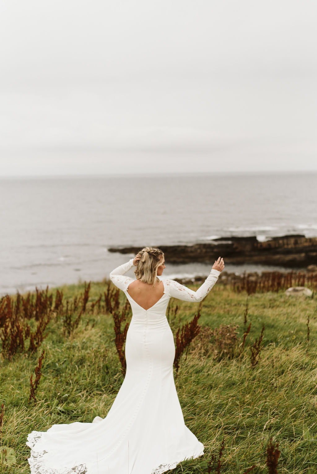 Back view of bride standing in front of Atlantic Ocean wearing a long sleeve crepe and lace wedding dress at Mullaghmore Head in Ireland