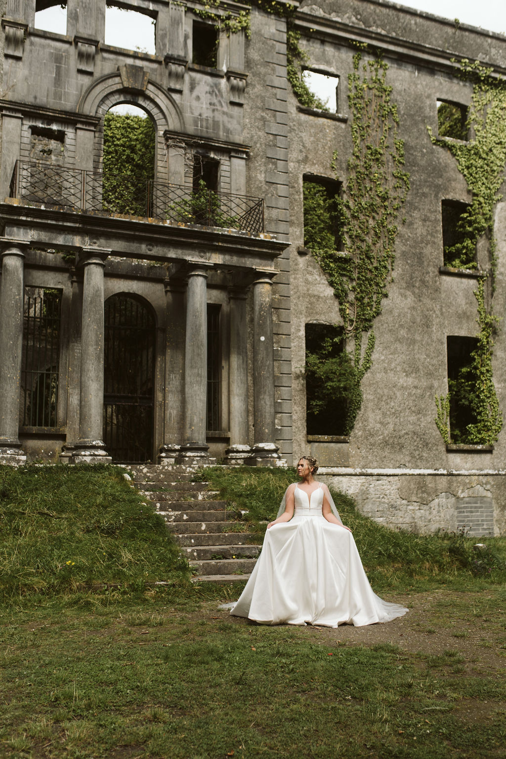 Bride stands in front of abandoned Moore Hall wearing a simple ballgown wedding dress with a plunging neckline in Ireland