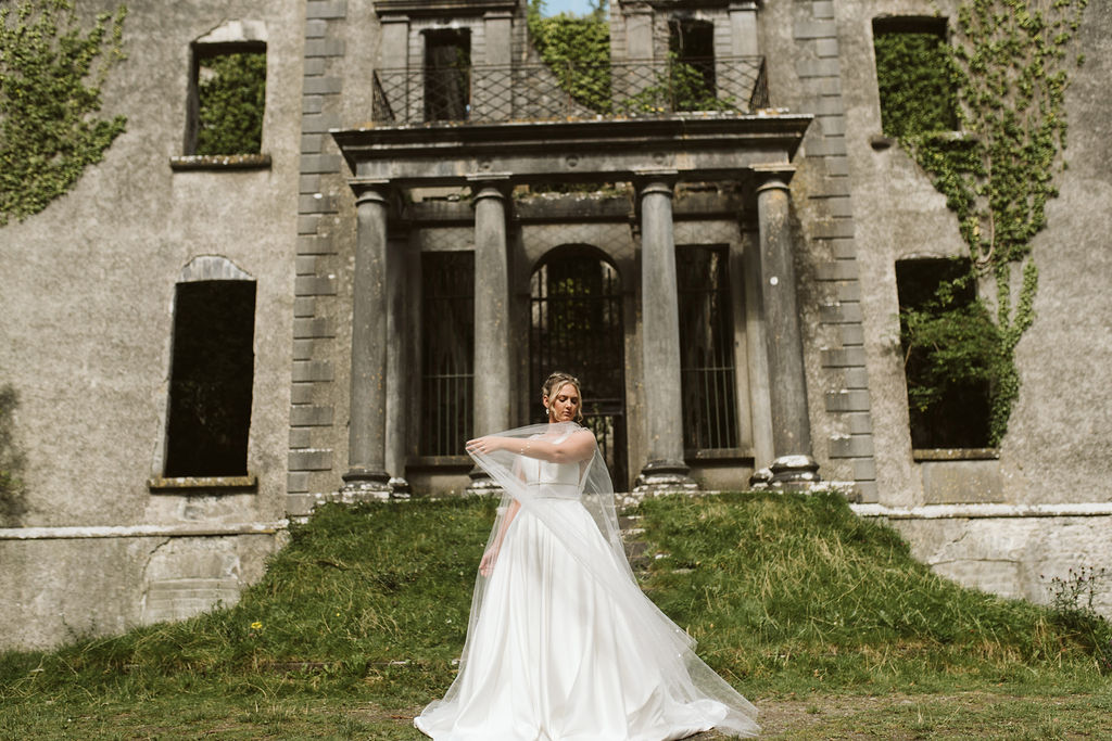 Bride plays with tulle cape wearing a simple ballgown wedding dress at Moore Hall in Ireland