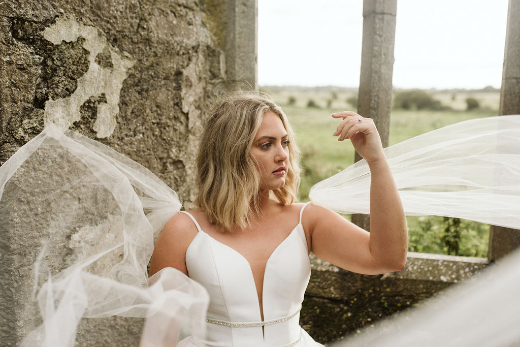 Close up image of bride's tulle wings blowing in the wind while wearing a deep plunge mikado ballgown wedding dress with straps and beaded banding at the waist at Ross Errilly Friary in Ireland