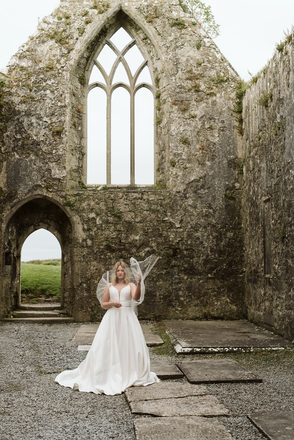 Wind blowing the tulle wings on a bride wearing a mikado ballgown wedding dress with beaded waist banding at Ross Errilly Friary in Ireland