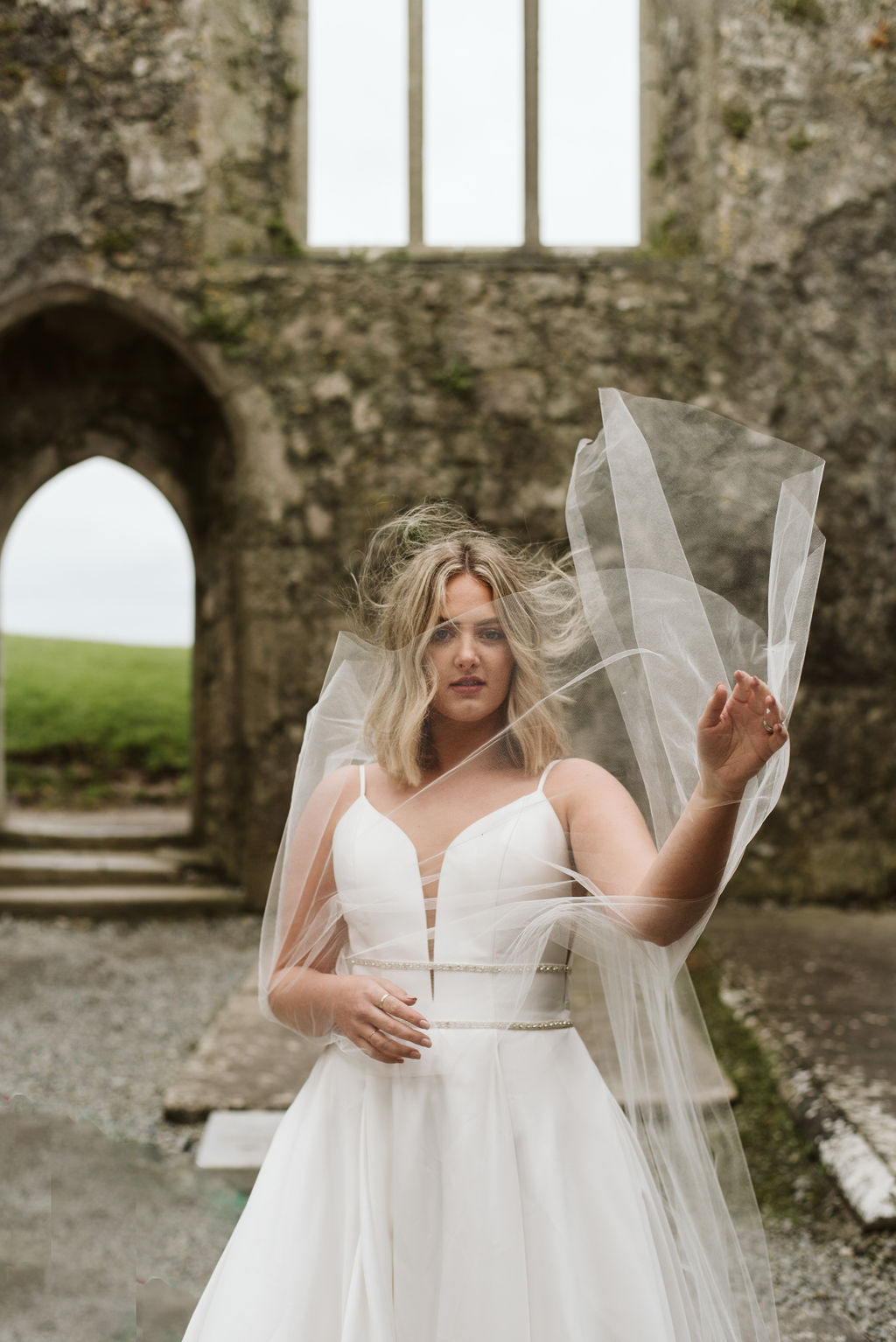tulle in front of bride's face at Ross Errilly Friary wearing mikado ballgown wedding dress with straps and a plunge neckline with beaded banding around the waist