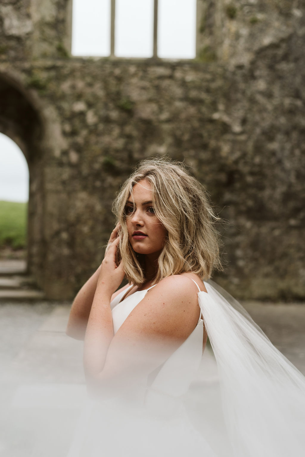 View of bride wearing a mikado ballgown wedding dress with straps through her tulle wings at Ross Errilly Friary in Ireland