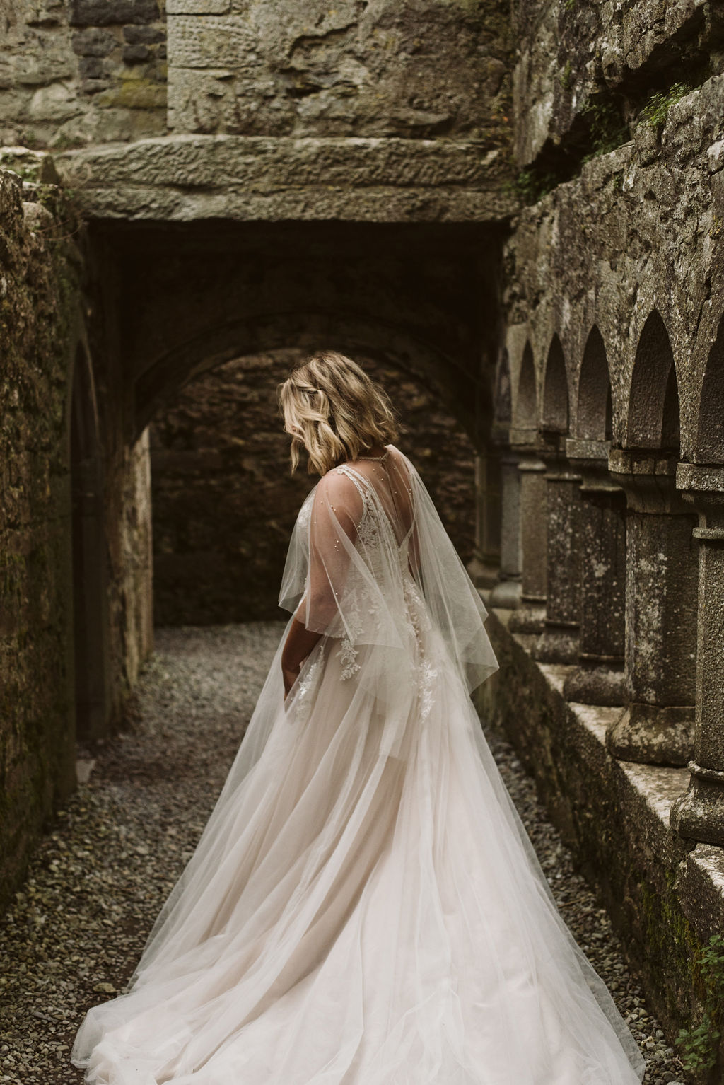 Back view of bride wearing a tulle and lace aline wedding dress with tulle cape at Ross Errilly Friary in Ireland