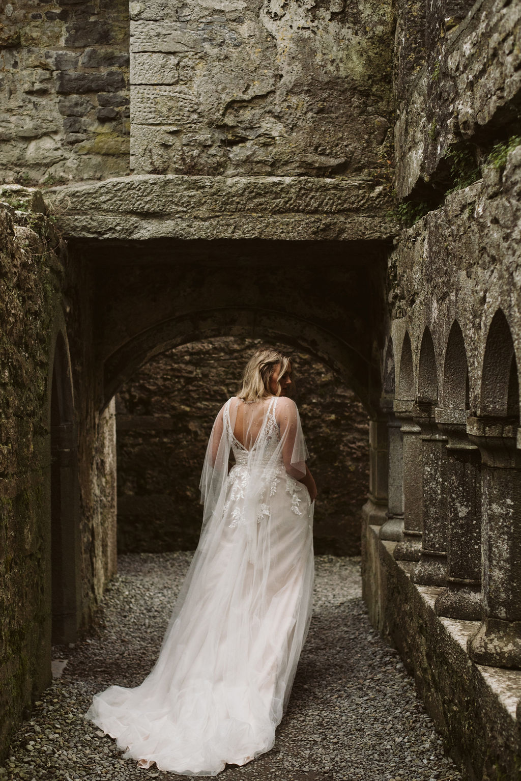 Back view of bride wearing a lace and tulle aline wedding dress and tulle cape at Ross Errilly Friary in Ireland