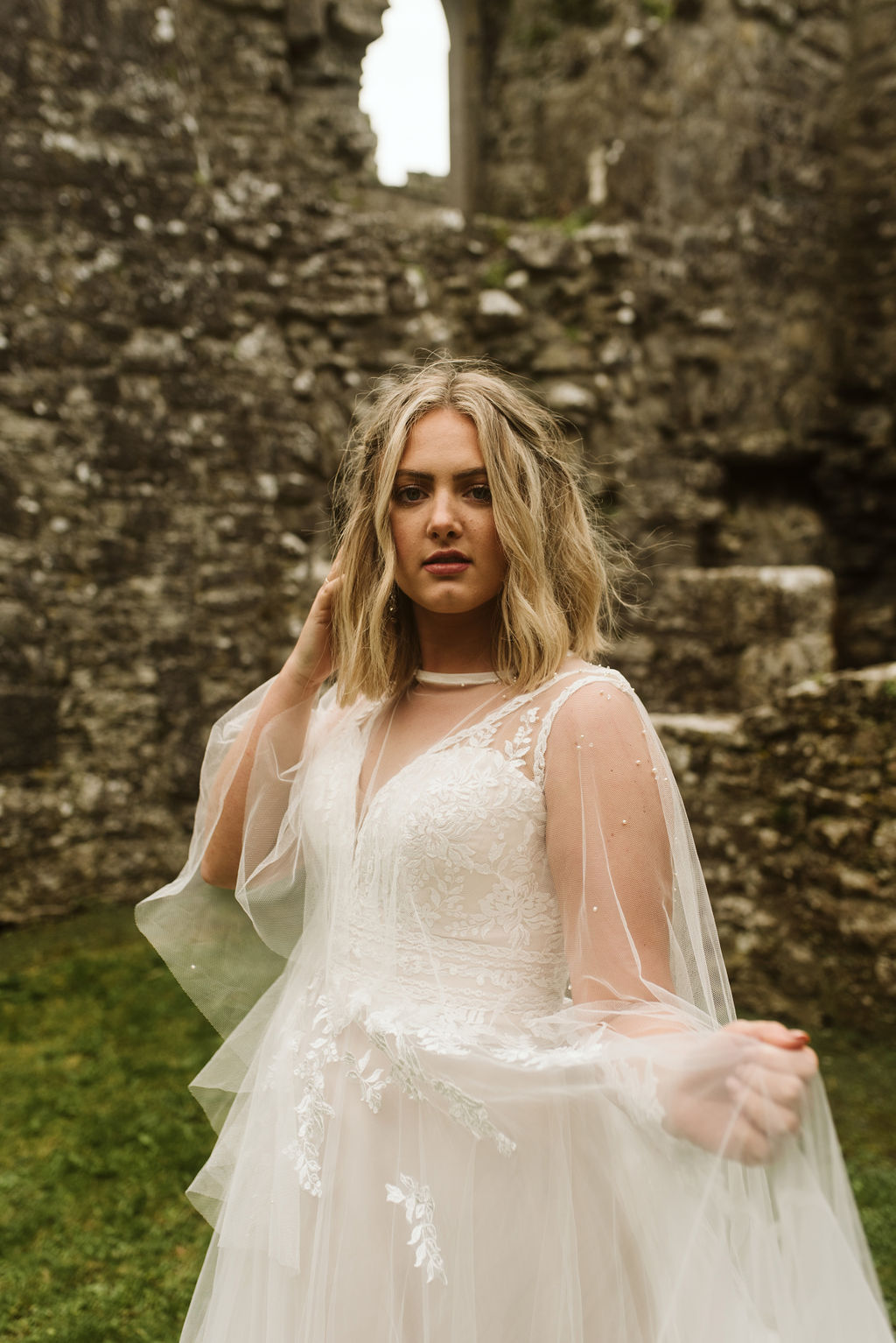 Close up view of a bride wearing a lace and tulle aline wedding dress with lace straps and a tulle cape at Ross Errilly Friary in Ireland