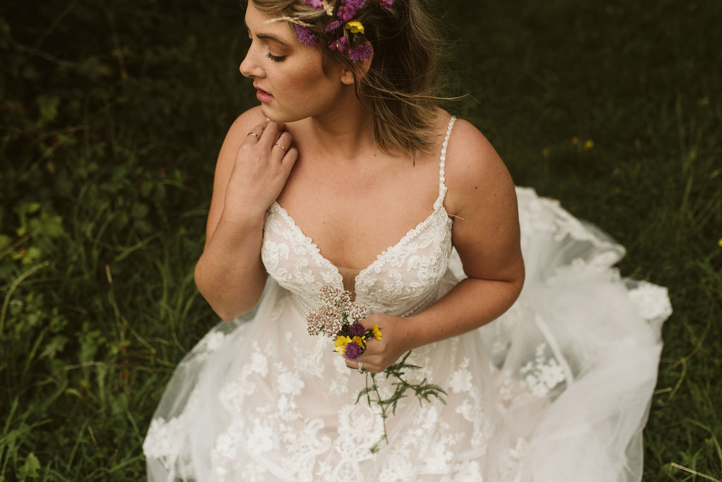 Bride with flowers in her hair wears a lace ballgown wedding dress with waist detail and straps next to Menlo Castle in Ireland