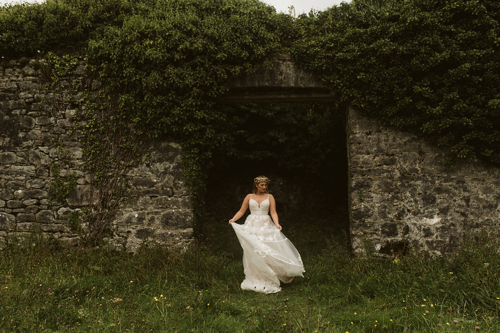 Bride twirls wearing a lace boho wedding dress with straps stands in front of the abandoned Menlo Castle in Ireland