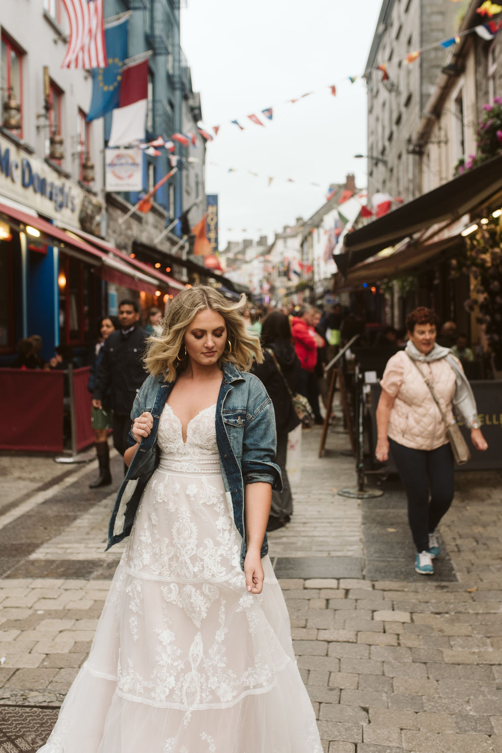 Bride wears a jean jacket and a lace boho wedding dress in the streets of Galway Ireland with people walking by