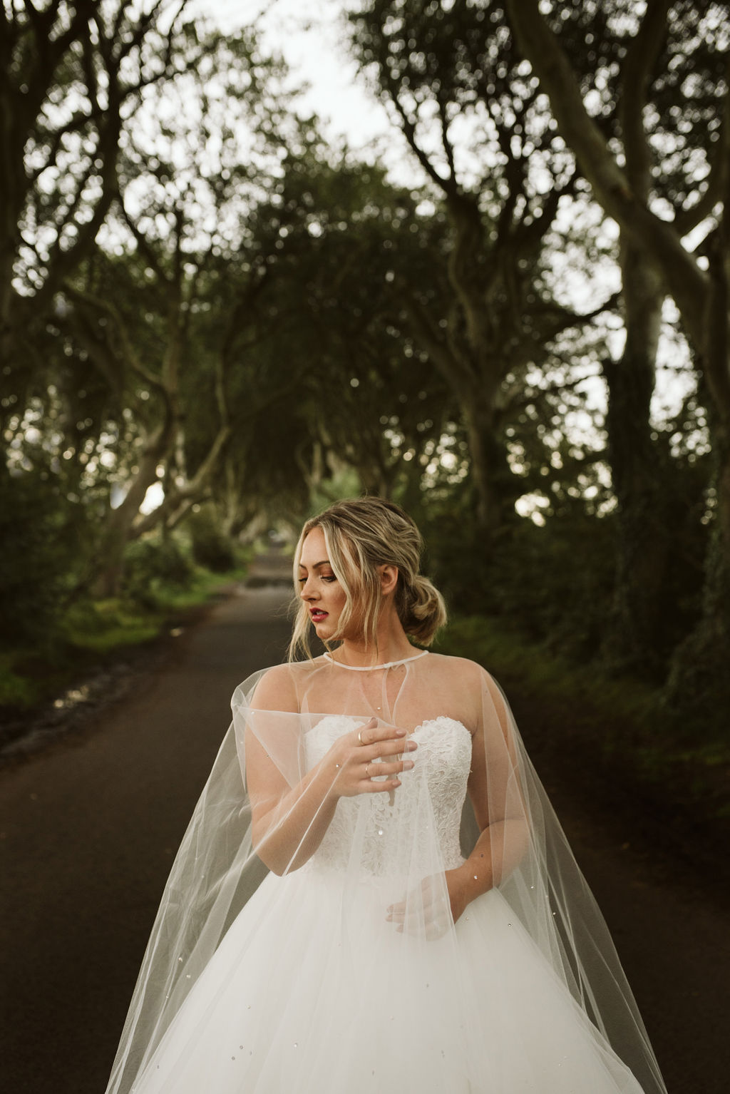 Bride wearing a lace and tulle horsehair ballgown wedding dress with a pearl and crystal tulle cape at The Dark Hedges in Northern Ireland