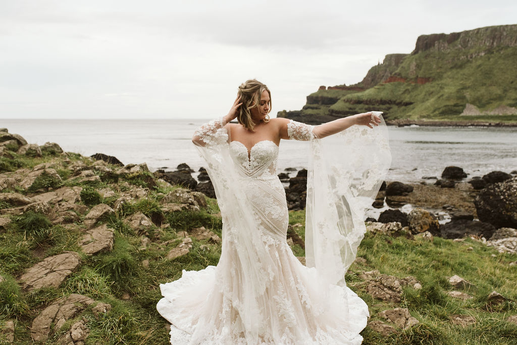 Bride wearing lace bell sleeves and a fitted lace boho wedding dress at Giant's Causeway in Northern Ireland
