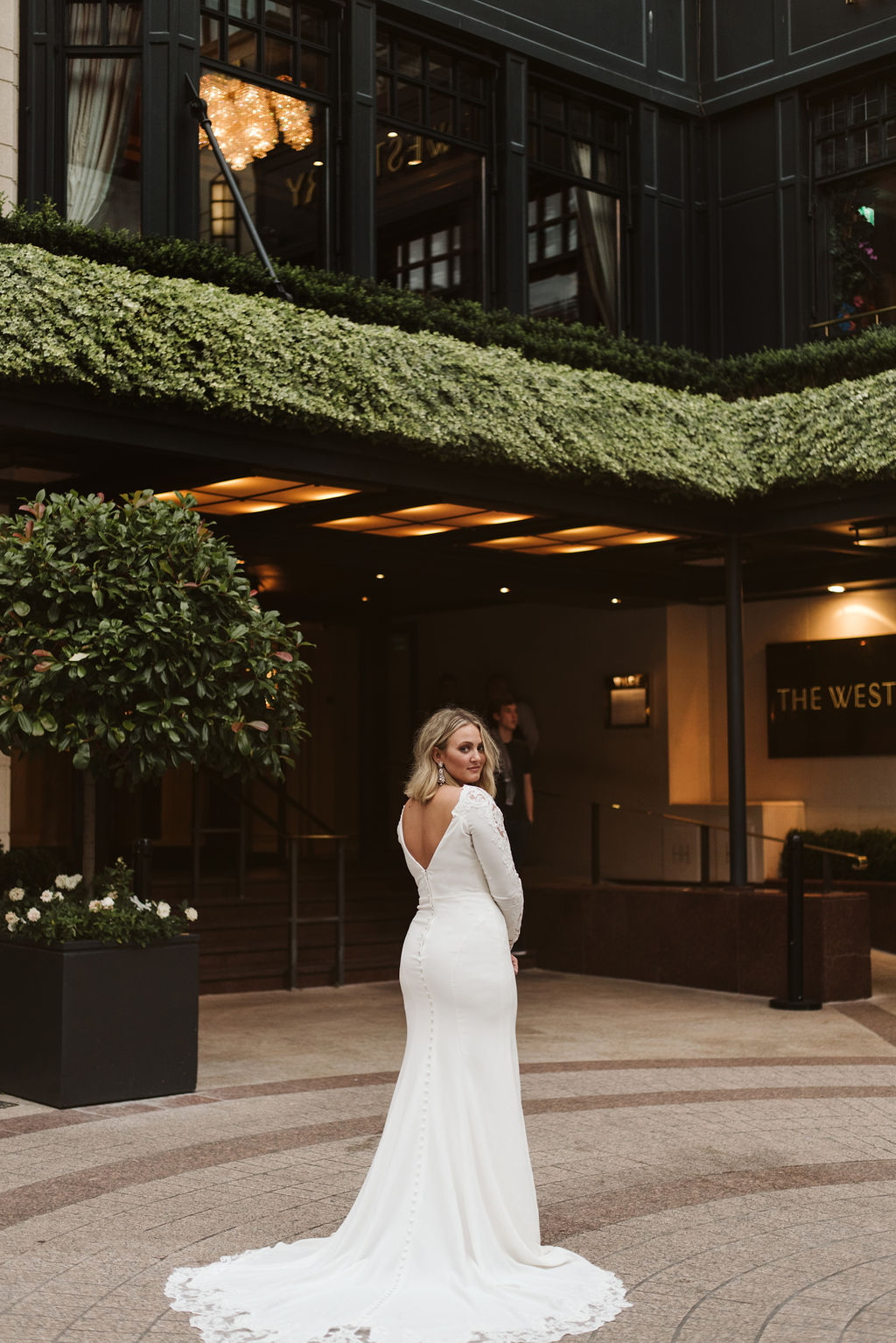 Bride in front of hotel in Dublin, Ireland wears a long sleeve simple wedding dress with lace detail