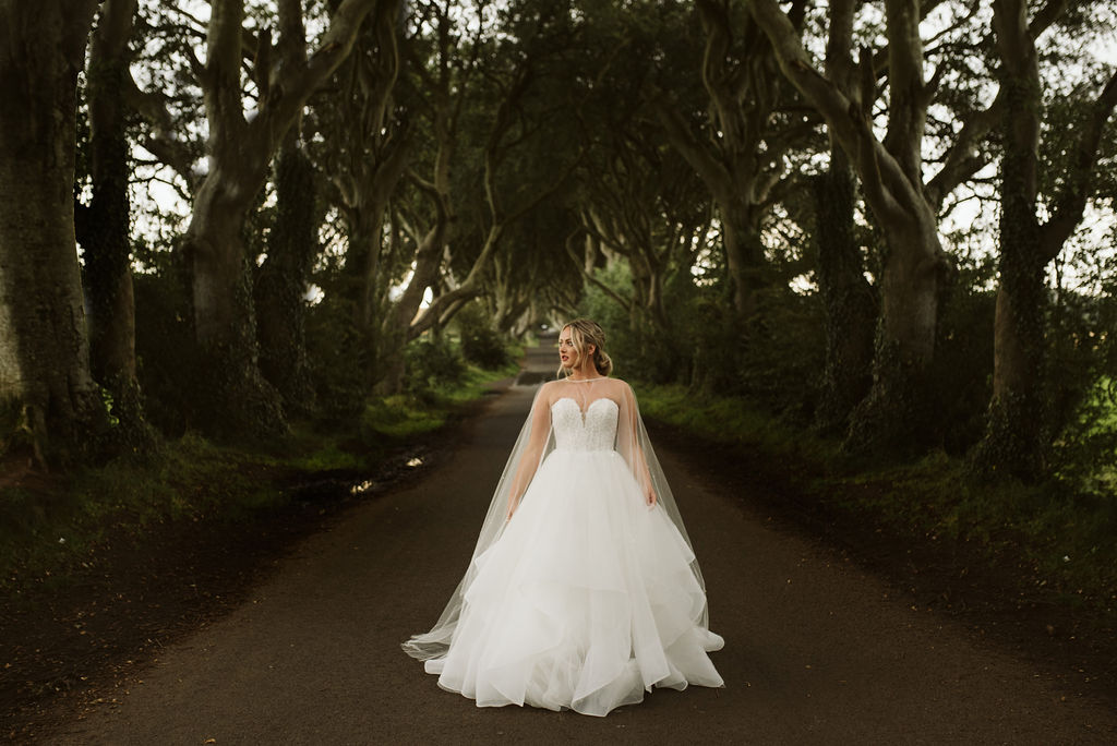 Bride wearing a lace and tulle horsehair ballgown wedding dress with a tulle cape with pearls and crystals at The Dark Hedges in Northern Ireland