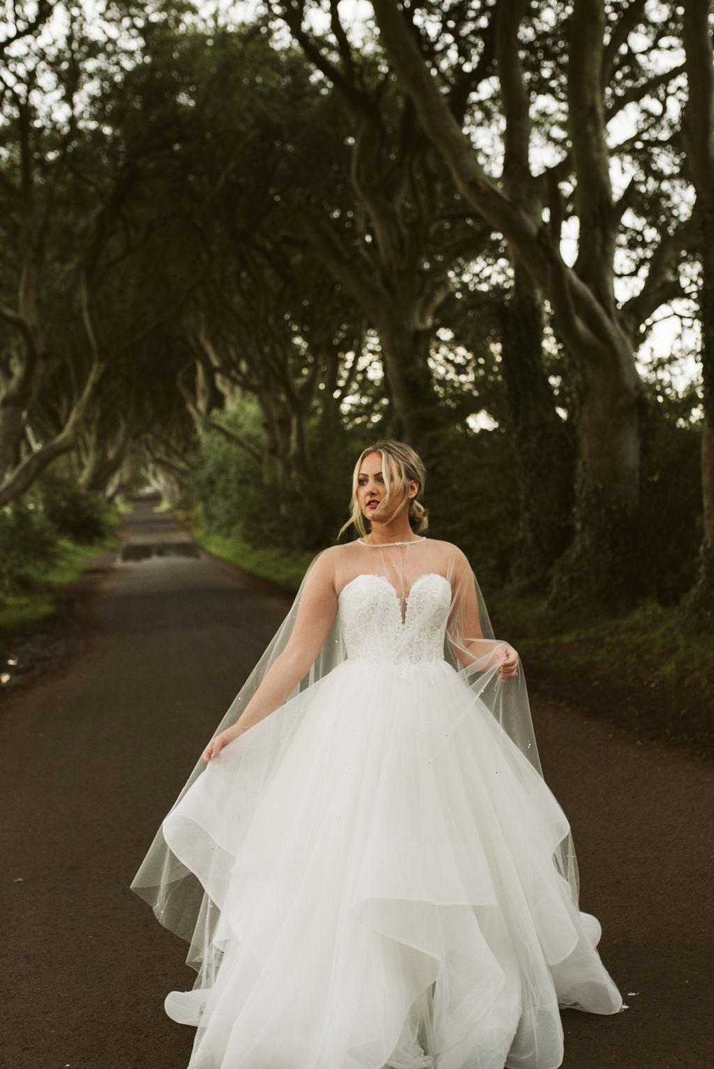 Bride wearing a lace and tulle horsehair ballgown wedding dress with a pearl and crystal tulle cape at The Dark Hedges in Northern Ireland