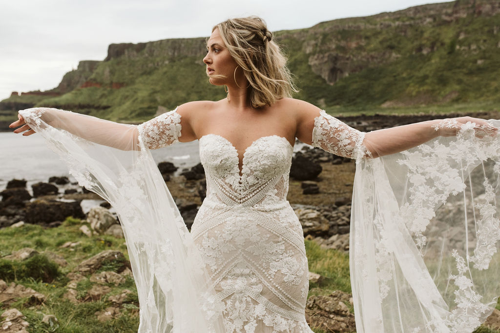 Bride wearing lace bell sleeves and a fitted lace boho wedding dress at Giant's Causeway in Northern Ireland