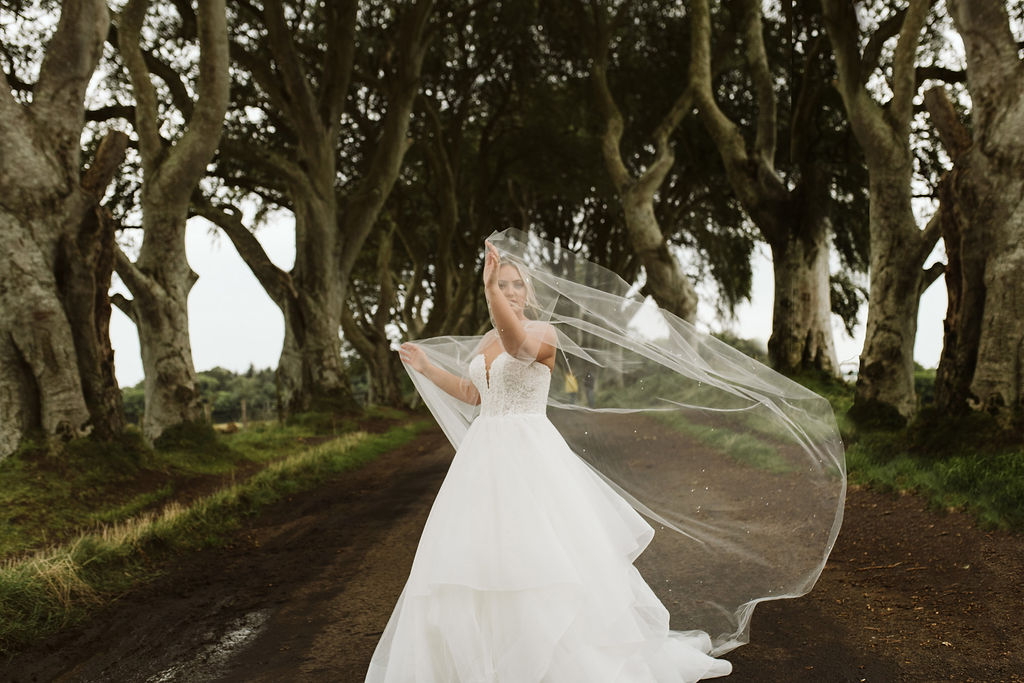 Sparkly tulle cape in front of bride's face wearing a lace and tulle horsehair ballgown wedding dress at The Dark Hedges in Northern Ireland