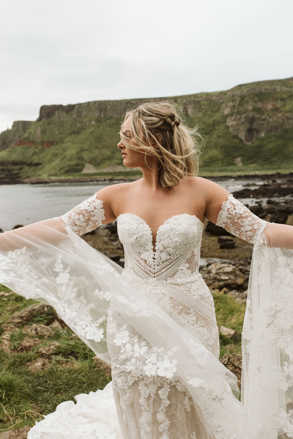 Bride plays with the lace bell sleeves of her fitted lace boho wedding dress at Giant's Causeway in Northern Ireland