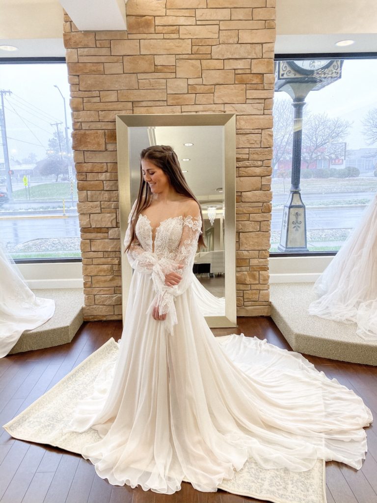Bride stands in a chiffon skirt ballgown with long romantic bell sleeves at One Fine Day Bridal and Gown Boutique in Fort Wayne, Indiana